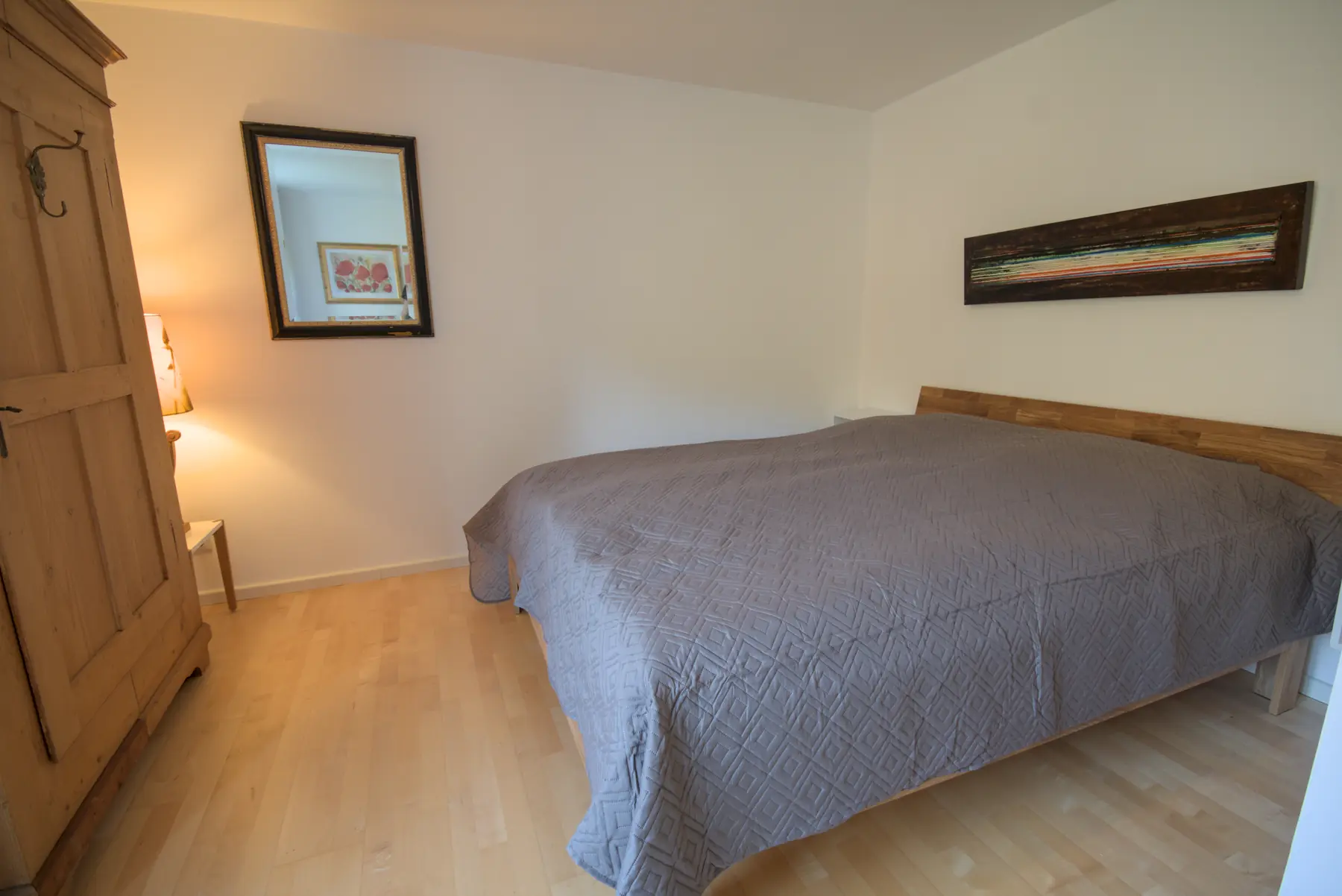 Das Schlafzimmer mit Doppelbett, hohem Holzschrank und Spiegel